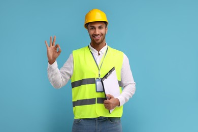 Photo of Engineer in hard hat showing ok gesture on light blue background