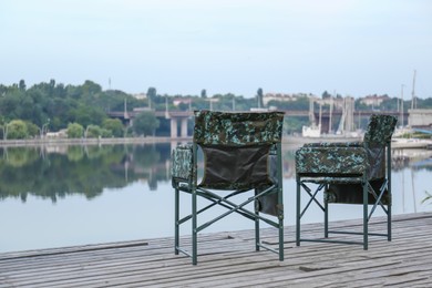 Photo of Camouflage fishing chairs on wooden pier near river