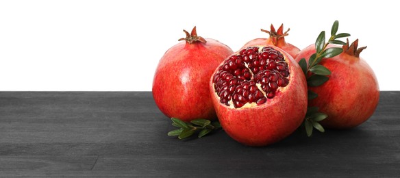 Photo of Fresh pomegranates and green leaves on black wooden table against white background, space for text