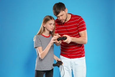 Photo of Emotional man and teenage girl playing video games with controllers on color background