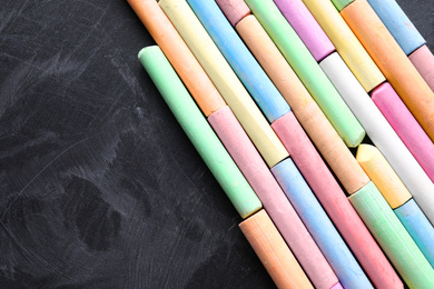 Photo of Pieces of color chalk on blackboard, flat lay. Space for text