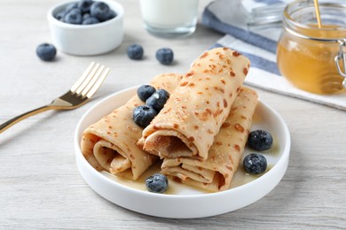 Photo of Delicious crepes with blueberries and honey on white wooden table