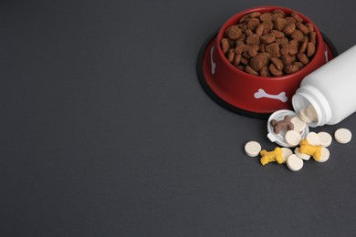 Photo of Bottle with vitamins and dry pet food in bowl on grey background, above view. Space for text