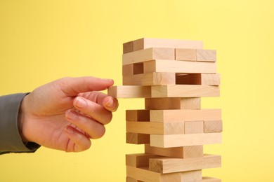 Photo of Woman playing Jenga tower on yellow background, closeup