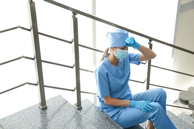 Photo of Exhausted doctor sitting on stairs in hospital. Stress of health care workers during COVID-19 pandemic