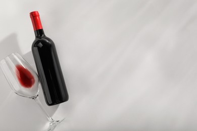 Photo of Bottle of expensive red wine and wineglass on light grey background, top view. Space for text
