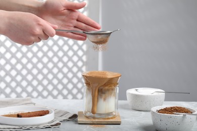 Photo of Woman sprinkling dalgona coffee with cinnamon at light gray table, closeup