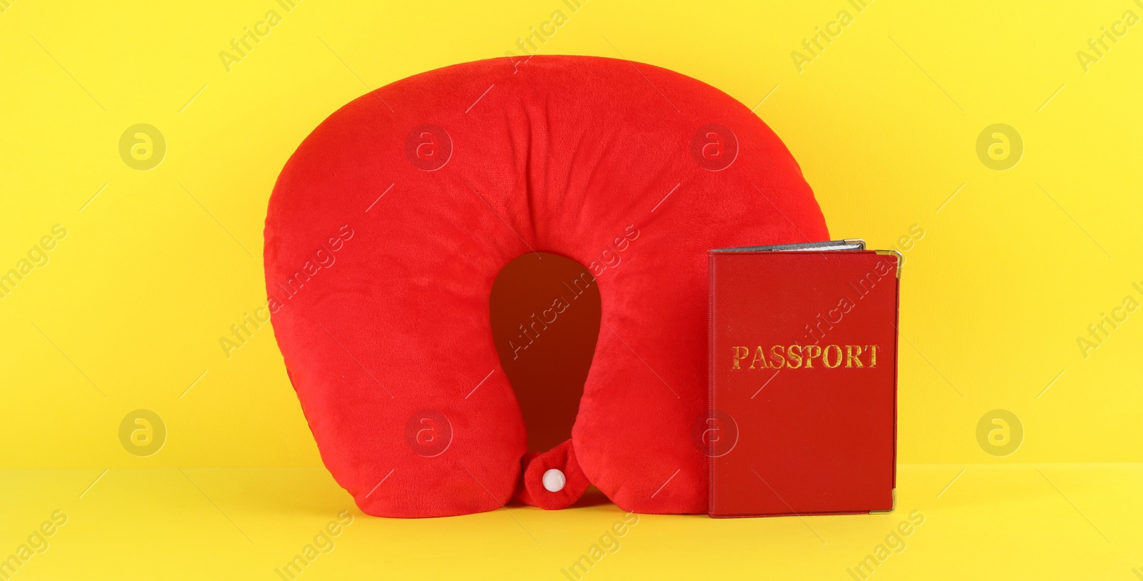 Photo of Red travel pillow and passport on yellow background