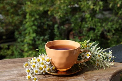 Photo of Cup of delicious chamomile tea and fresh flowers outdoors on sunny day