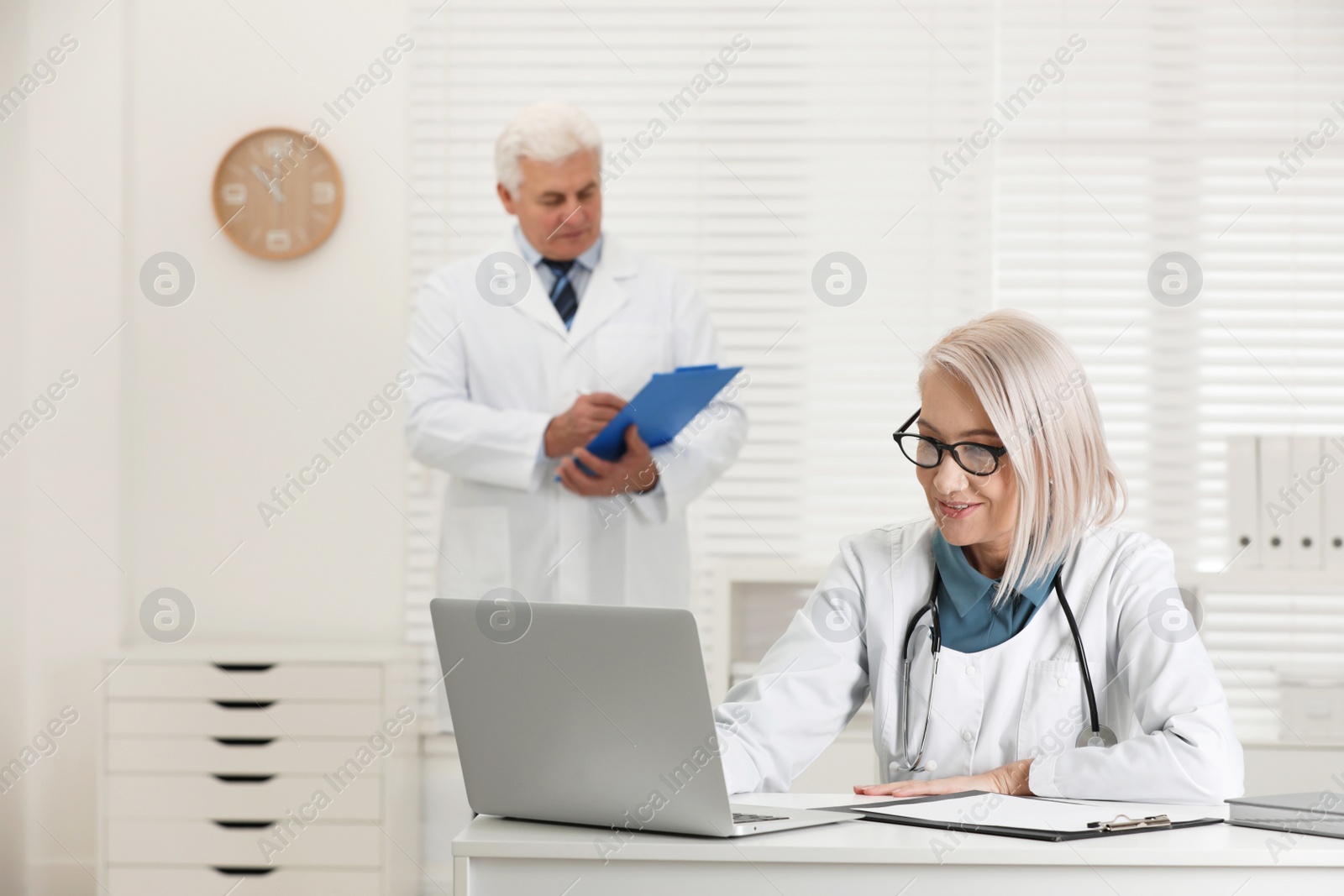 Photo of Mature female doctor working with laptop at table in office