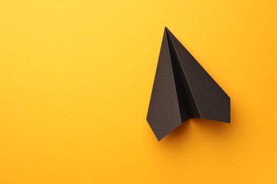 Photo of Handmade black paper plane on yellow background, top view. Space for text