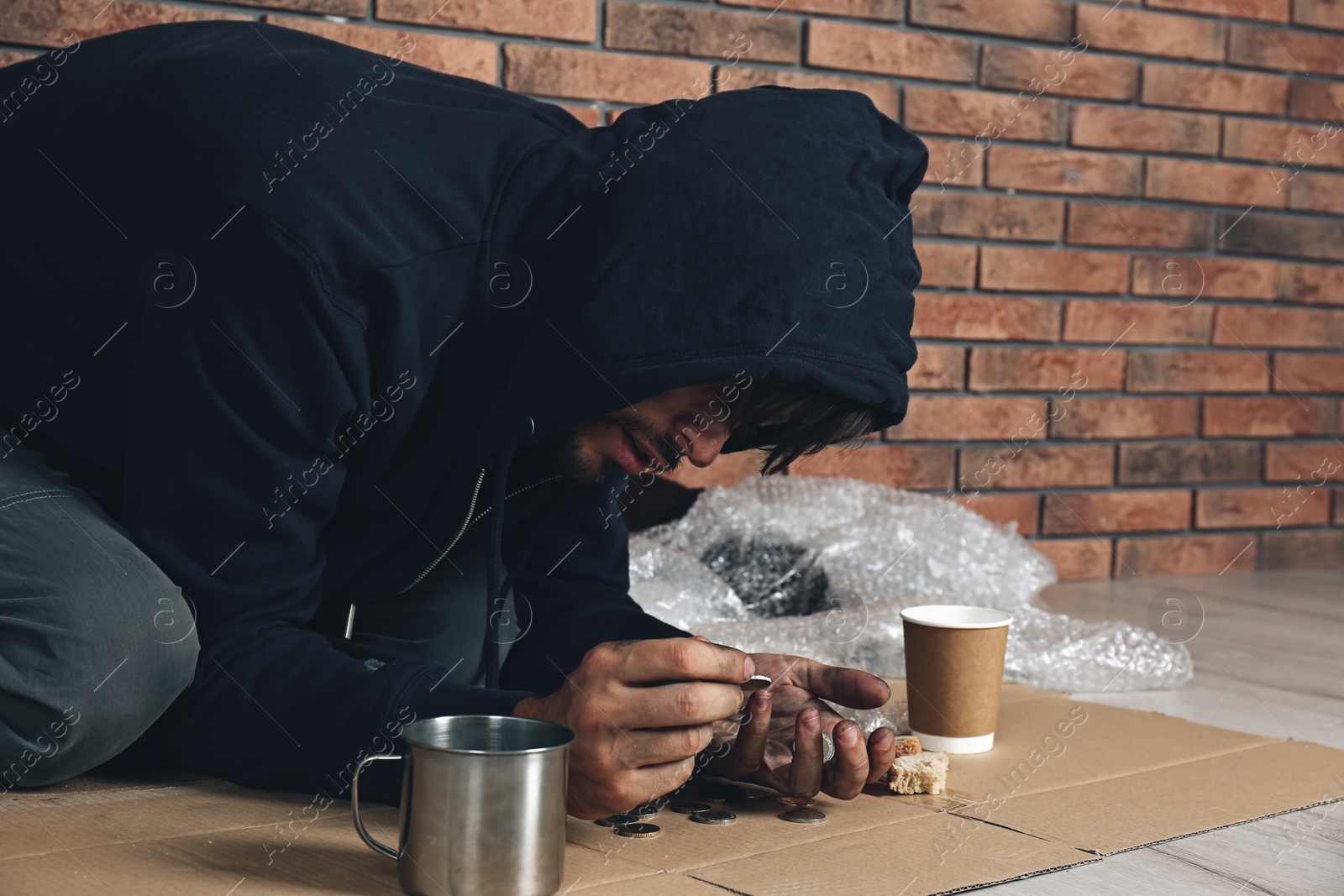 Image of Poor man counting coins on floor near brick wall