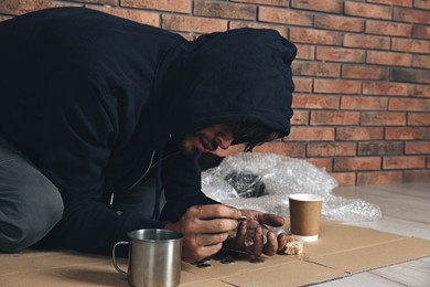 Image of Poor man counting coins on floor near brick wall