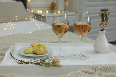 Photo of Tray with glasses of wine and cookies in bedroom adorned for romantic date