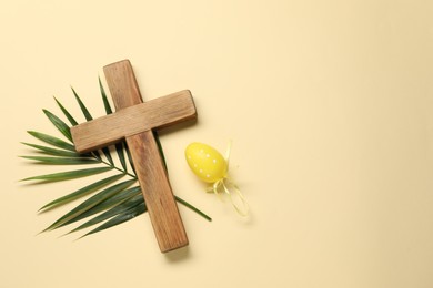 Photo of Wooden cross, painted Easter egg and palm leaf on beige background, top view. Space for text