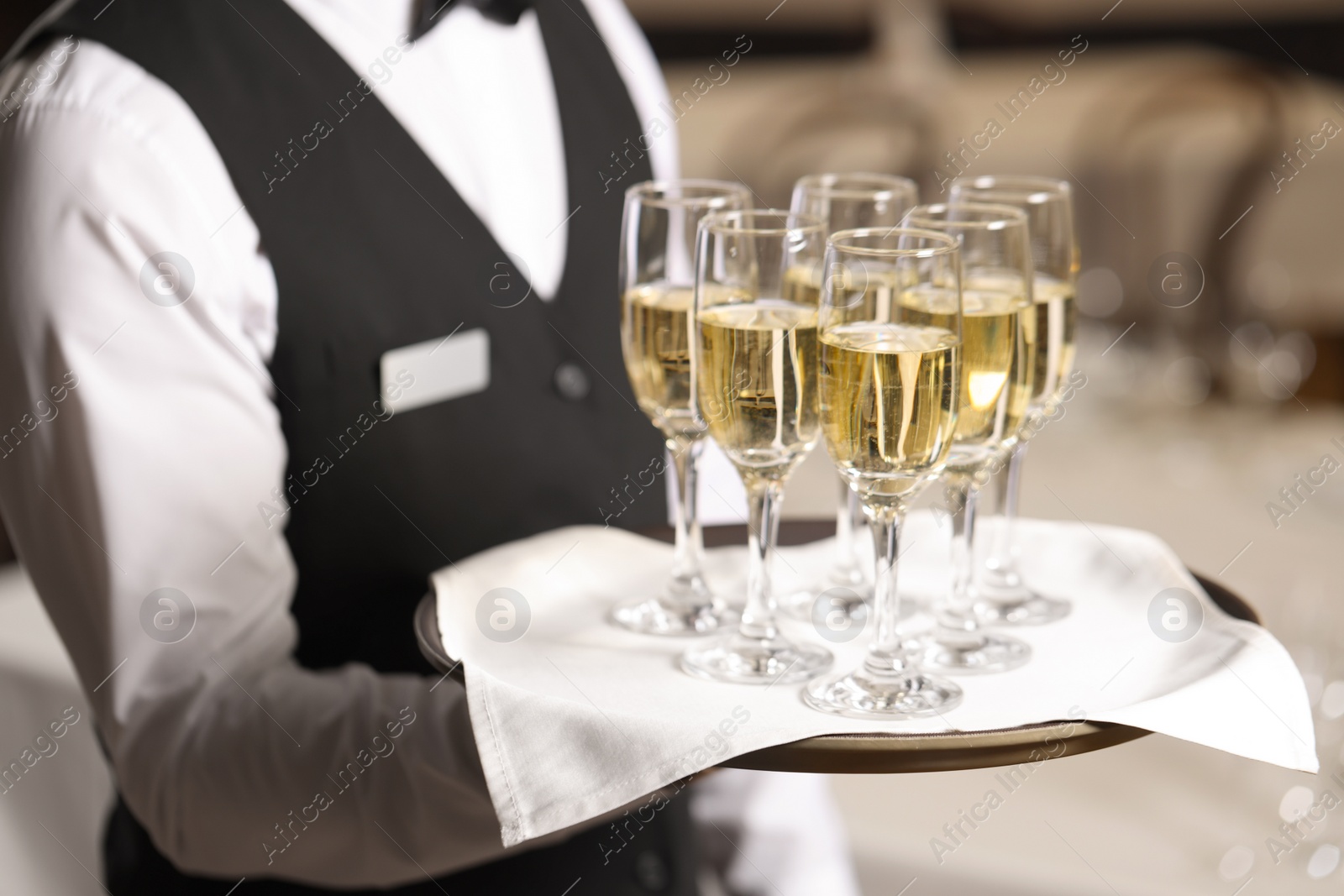 Photo of Butler holding tray with glasses of sparkling wine in restaurant, closeup