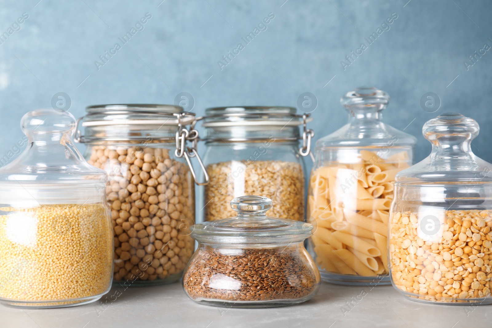 Photo of Jars with different cereals on grey marble table against light blue background