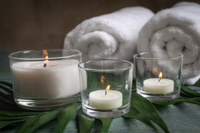 Photo of Spa composition with burning wax candles, towels and tropical leaf on table