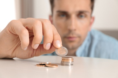 Photo of Young man stacking coins at table, focus on hand