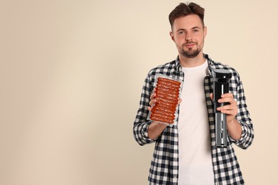 Photo of Man holding sous vide cooker and sausages in vacuum pack on beige background, space for text
