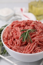 Photo of Fresh raw ground meat and rosemary in bowl on table, closeup