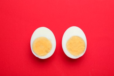 Photo of Halves of fresh hard boiled egg on red background, flat lay