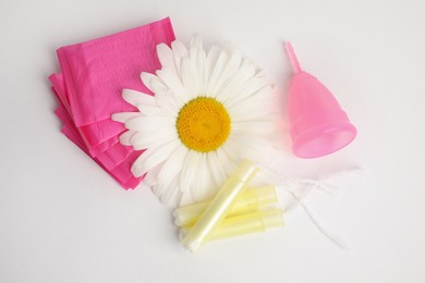 Photo of Tampons, pads, menstrual cup and chamomile flower on white background, top view