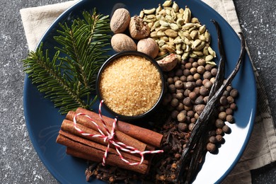 Photo of Plate with different aromatic spices and fir branches on grey textured table, top view