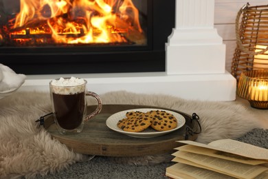 Photo of Open book, hot drink and cookies near decorative fireplace in room. Cozy home atmosphere