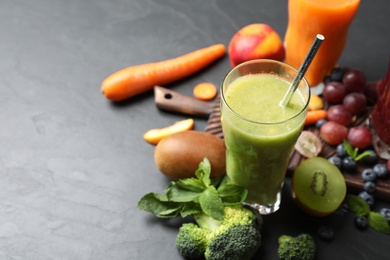 Photo of Delicious colorful juice in glass and fresh ingredients on black table, space for text