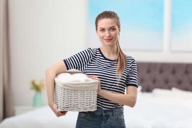 Woman holding wicker basket with folded clean towels in bedroom. Laundry day