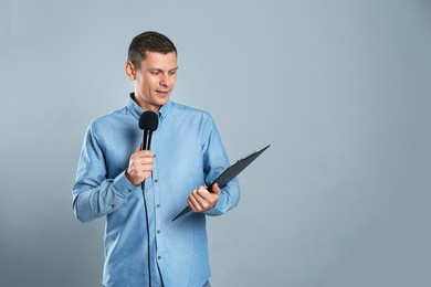 Photo of Male journalist with microphone and clipboard on grey background. Space for text