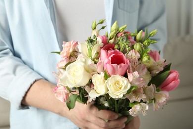 Photo of Man holding bouquet of beautiful flowers indoors, closeup