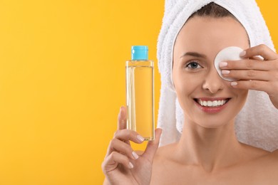 Photo of Smiling woman removing makeup with cotton pad and holding bottle on yellow background. Space for text