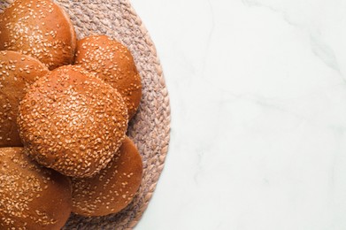 Photo of Fresh buns with sesame seeds on white marble table, flat lay. Space for text