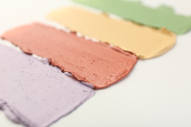 Photo of Samples of different color correcting concealers on white background, closeup