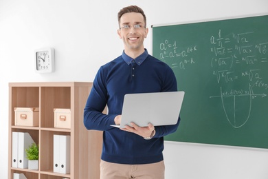 Photo of Young male teacher with laptop standing in classroom