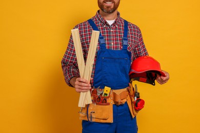 Photo of Professional builder in uniform with wooden bars and tool belt on yellow background, closeup