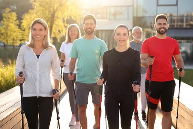 Photo of Group of people practicing Nordic walking with poles outdoors on sunny day
