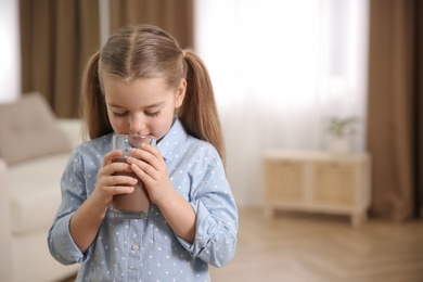 Photo of Cute little child drinking tasty chocolate milk at home, space for text