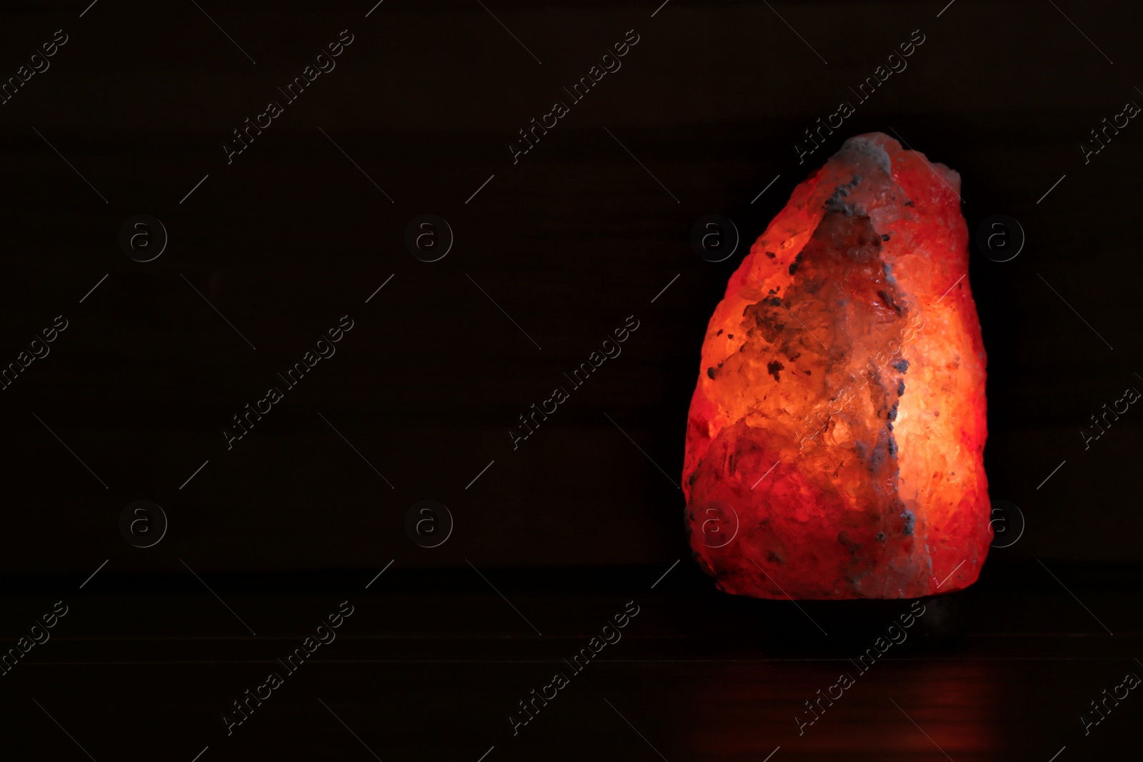 Photo of Himalayan salt lamp glowing on dark background with space for text