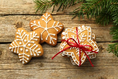 Photo of Tasty Christmas cookies with icing and fir tree branches on wooden table, flat lay