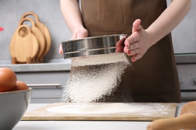 Photo of Woman sieving flour at table in kitchen, closeup