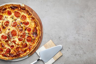 Photo of Delicious homemade prosciutto quiche and spatula on light gray table, flat lay. Space for text