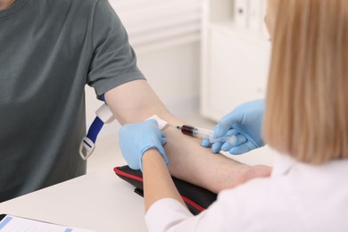 Photo of Doctor taking blood sample from patient with syringe at white table in hospital, closeup