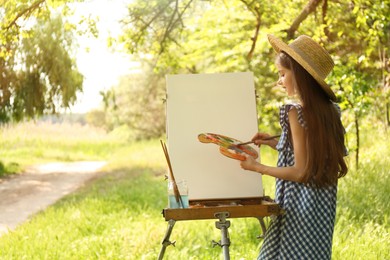 Photo of Little girl painting on easel in picturesque countryside