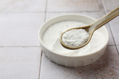 Photo of Spoon of baking powder over bowl at light tiled table, closeup. Space for text
