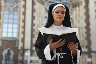 Photo of Young nun reading Bible near cathedral outdoors. Space for text