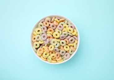 Photo of Tasty cereal rings in bowl on light blue table, top view