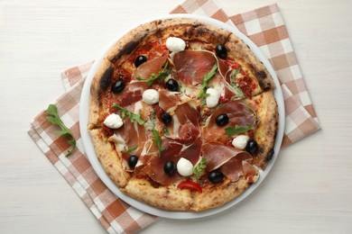 Photo of Tasty pizza with cured ham, olives, mozzarella cheese, sun-dried tomato and arugula on light wooden table, top view